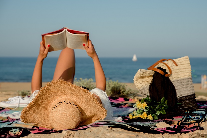 Eine Frau mit Sonnenhut liest ein Buch am Strand auf einer Decke